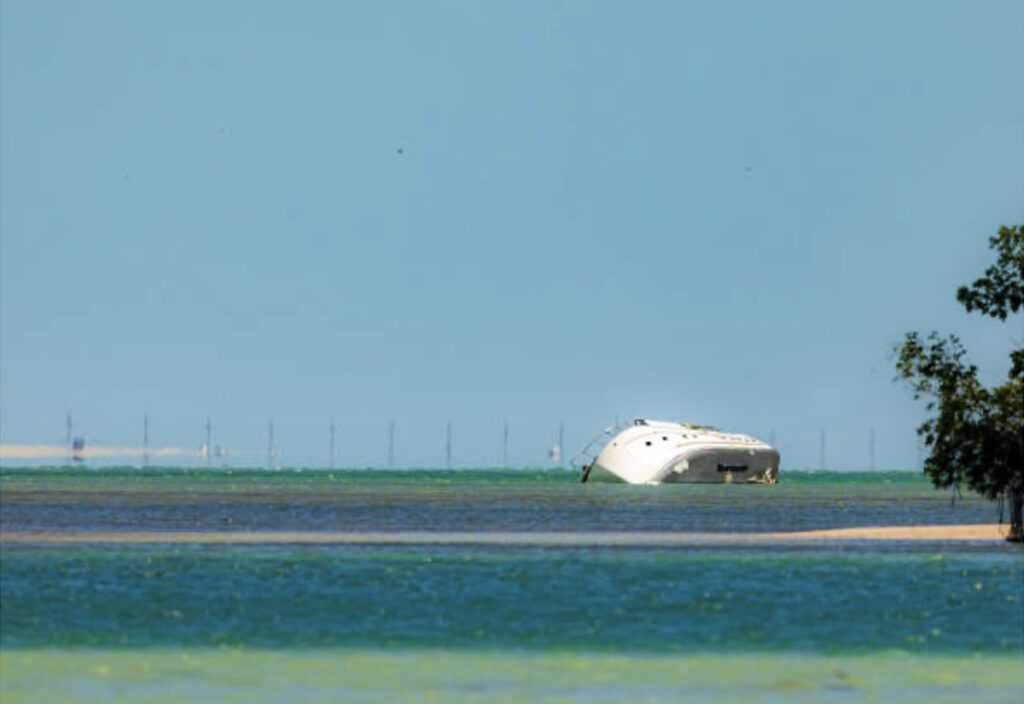 A partially submerged white yacht tilts in shallow blue and green water under a clear blue sky.